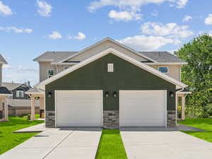 View of front of house featuring a front lawn, concrete driveway, a garage, and stone siding