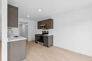 Kitchen featuring stainless steel appliances, light wood-style floors, dark brown cabinetry, recessed lighting, and light stone counters