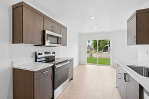 Kitchen featuring stainless steel appliances, light wood-type flooring, light stone countertops, and modern cabinets