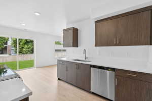 Kitchen with stainless steel dishwasher, light wood-type flooring, modern cabinets, light stone countertops, and dark brown cabinetry