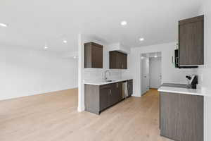 Kitchen featuring dark brown cabinets, light wood-style flooring, appliances with stainless steel finishes, recessed lighting, and light stone countertops