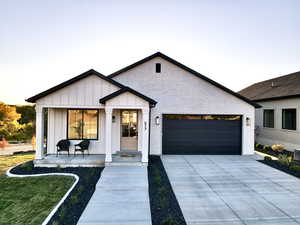 Modern farmhouse featuring board and batten siding, an attached garage, driveway, brick siding, and a front yard