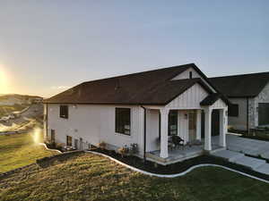 Back of property featuring a porch, a shingled roof, a lawn, board and batten siding, and concrete driveway