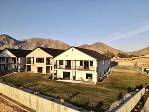 Back of property with a balcony, a patio, a mountain view, and a lawn