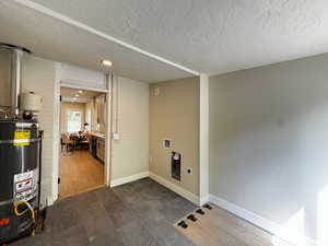 Laundry room featuring secured water heater, brick wall, a textured ceiling, and hookup for a washing machine