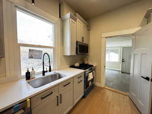 Kitchen with appliances with stainless steel finishes, light wood finished floors, and light stone countertops