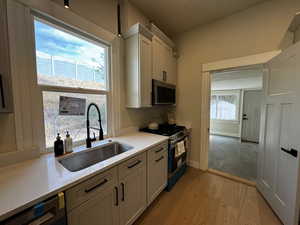 Kitchen with stainless steel appliances, light wood-type flooring, light stone counters, and white cabinetry