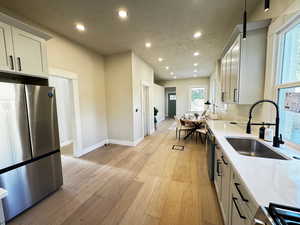 Kitchen with stainless steel appliances, recessed lighting, light wood-type flooring, light stone countertops, and white cabinetry