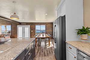 Kitchen featuring a textured ceiling, hanging light fixtures, light stone countertops, freestanding refrigerator, and dark wood-style floors