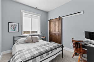 Bedroom with light colored carpet, a barn door, and a desk