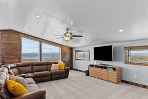 Living room with a textured ceiling, light colored carpet, wood walls, lofted ceiling, and ceiling fan