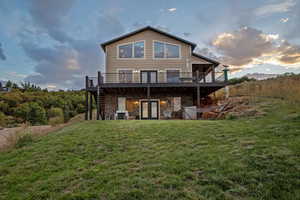 Back of house at dusk featuring stone siding, a lawn, a wooden deck, and a patio