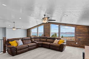 Living area featuring carpet, a textured ceiling, lofted ceiling, wood walls, and a water view