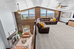 Living area featuring ceiling fan, light colored carpet, wooden walls, a textured ceiling, and vaulted ceiling
