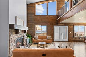 Living area with a fireplace, wood finished floors, wooden walls, a towering ceiling, and french doors