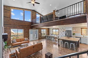 Living room with light wood-style floors, high vaulted ceiling, a ceiling fan, wood walls, and recessed lighting