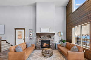 Living area with wooden walls, a high ceiling, a stone fireplace, and stairs