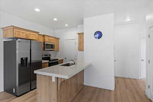 Kitchen with stainless steel appliances, light wood finished floors, light brown cabinetry, a peninsula, and recessed lighting