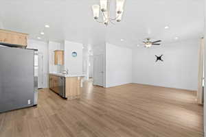 Kitchen featuring light brown cabinetry, stainless steel appliances, light countertops, open floor plan, and a chandelier