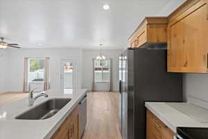 Kitchen with light wood-style flooring, decorative light fixtures, brown cabinets, a chandelier, and stainless steel appliances