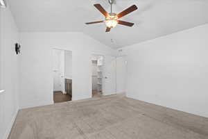 Unfurnished bedroom with lofted ceiling, carpet floors, a spacious closet, ceiling fan, and connected bathroom