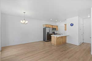 Kitchen featuring appliances with stainless steel finishes, a peninsula, light countertops, a breakfast bar area, and light wood finished floors