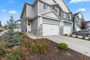 View of front facade with stone siding, an attached garage, driveway, and board and batten siding