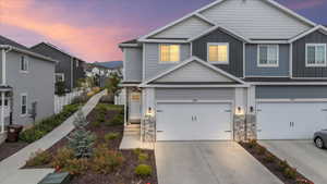 View of front facade with board and batten siding, a garage, concrete driveway, and stone siding