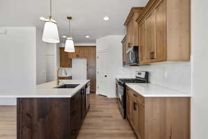 Kitchen with appliances with stainless steel finishes, brown cabinets, hanging light fixtures, an island with sink, and recessed lighting