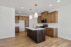 Kitchen featuring decorative light fixtures, brown cabinets, stainless steel appliances, decorative backsplash, and a center island with sink