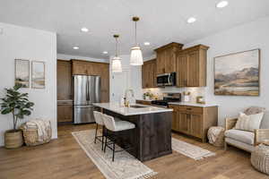 Kitchen with a breakfast bar, appliances with stainless steel finishes, an island with sink, hanging light fixtures, and recessed lighting