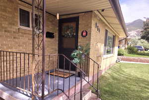 Entrance to property with brick siding, a porch, a lawn, and a mountain view