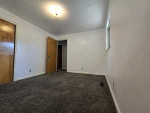 Unfurnished bedroom with dark carpet, a textured ceiling, and a closet