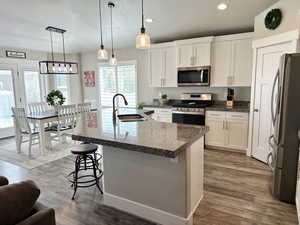 Kitchen with white cabinets, stainless steel appliances, hanging light fixtures, dark wood finished floors, and recessed lighting