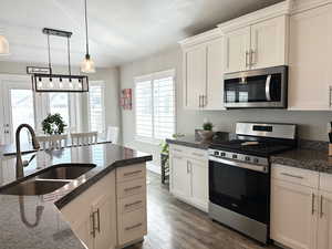 Kitchen featuring stainless steel appliances, dark wood-style flooring, hanging light fixtures, white cabinets, and a textured ceiling