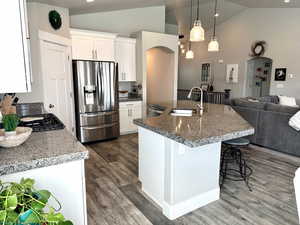 Kitchen featuring lofted ceiling, appliances with stainless steel finishes, open floor plan, white cabinetry, and hanging light fixtures