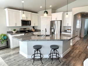 Kitchen featuring arched walkways, appliances with stainless steel finishes, pendant lighting, a kitchen island with sink, and a kitchen breakfast bar