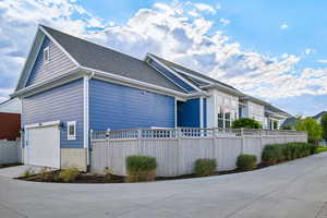 View of side of home with a fenced front yard, driveway, a shingled roof, and an attached garage