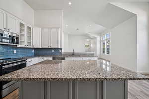 Kitchen with appliances with stainless steel finishes, light wood-type flooring, recessed lighting, glass insert cabinets, and light stone countertops