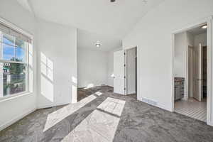 Unfurnished bedroom featuring carpet floors, lofted ceiling, ensuite bathroom, and ceiling fan