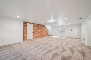 Below grade area with light carpet, recessed lighting, and brick wall