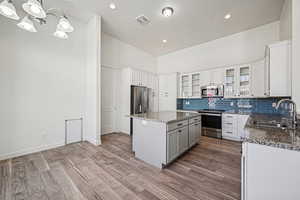 Kitchen with stainless steel appliances, glass insert cabinets, gray cabinetry, light stone countertops, and tasteful backsplash