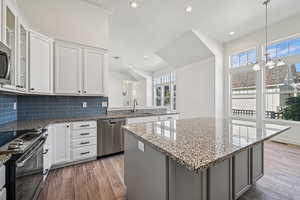 Kitchen featuring recessed lighting, white cabinets, a kitchen island, light stone counters, and appliances with stainless steel finishes