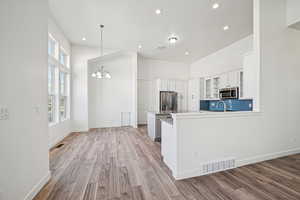 Kitchen with glass insert cabinets, white cabinets, decorative backsplash, hanging light fixtures, and a peninsula