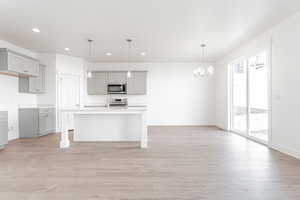 Kitchen featuring gray cabinets, hanging light fixtures, a breakfast bar, a center island with sink, and light wood-type flooring