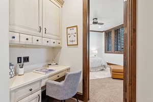 Office with built in study area, light colored carpet, and a ceiling fan