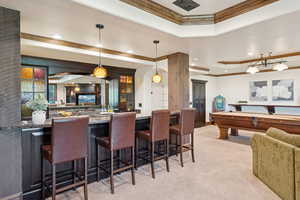 Indoor bar featuring a raised ceiling, crown molding, pendant lighting, recessed lighting, and light colored carpet