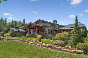 View of front of property featuring a front lawn, stone siding, a chimney, and a porch