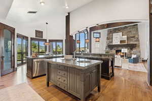 Kitchen featuring pendant lighting, open floor plan, dark stone counters, a stone fireplace, and light wood-type flooring