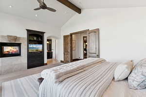Bedroom with light colored carpet, beamed ceiling, a fireplace, a ceiling fan, and arched walkways